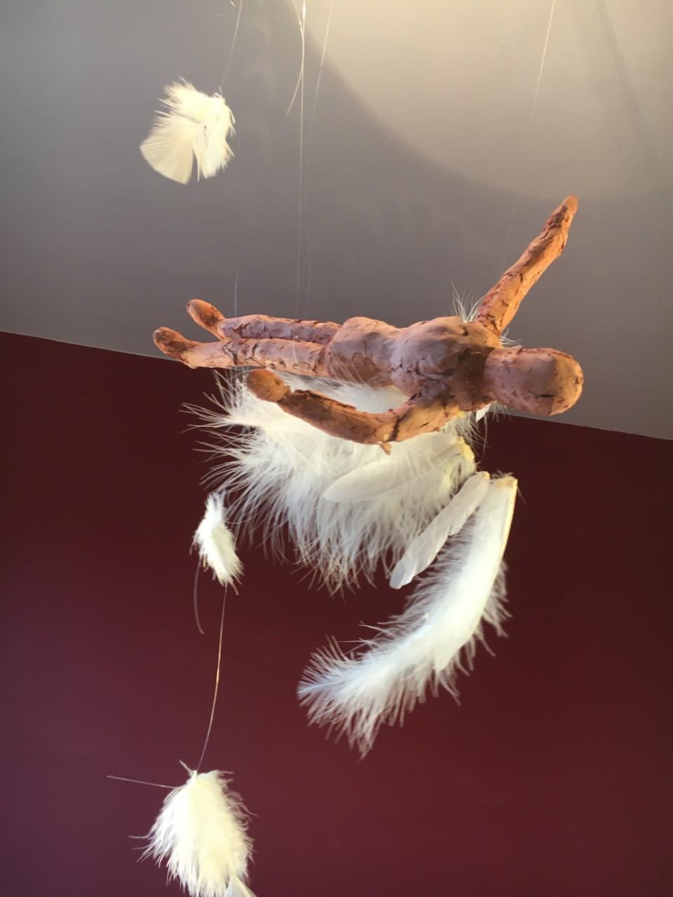 A suspended sculpture of Icarus with the feathers of his wings falling off.