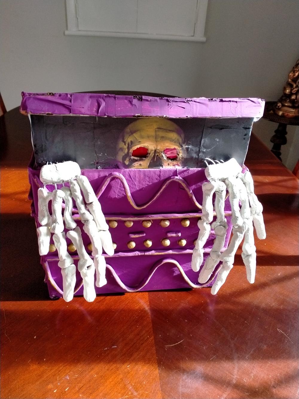 Model of Pandora's Box: skeleton emerges from beneath the half-open lid of a purple box.