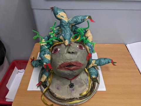 A papier-mâché Medusa head with a piercing yet sympathetic gaze, crowned with glossy snakes and pipe cleaners.